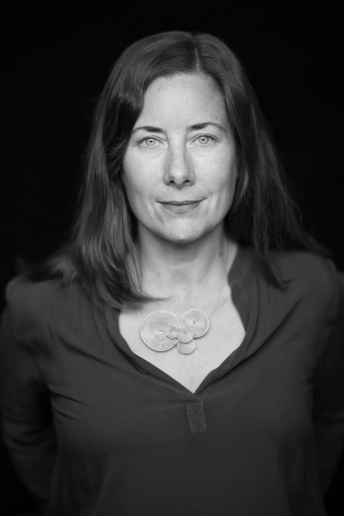 Jennifer Redfearn looking straight at the camera. She has shoulder-length hair and is wearing a necklace and black button-down shirt. Portrait in black and white.