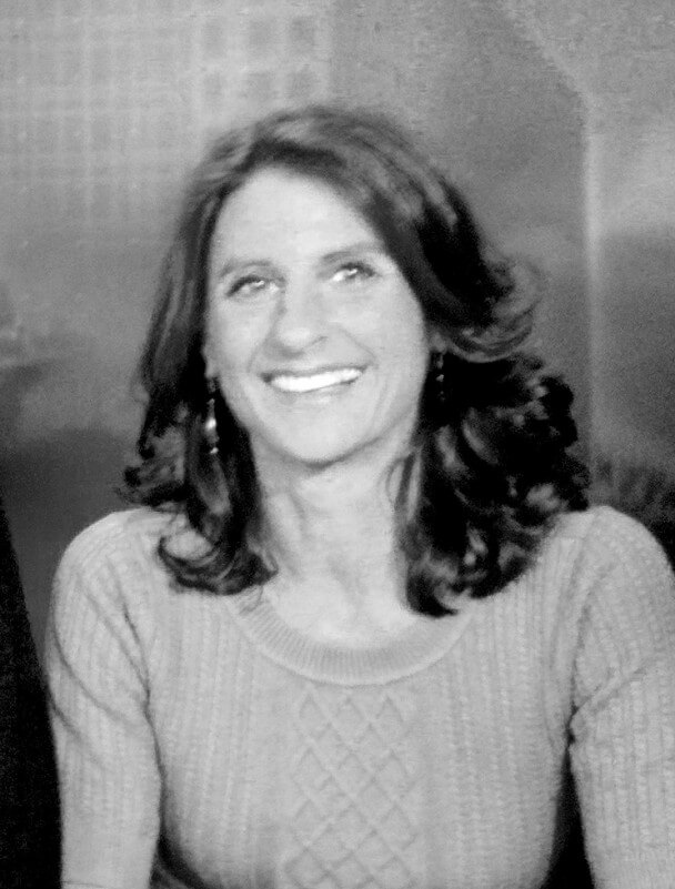 Jill Bauer looking straight ahead and smiling. She has shoulder-length, dark and wavy hair and is wearing a light-colored sweater. Black and white portrait.
