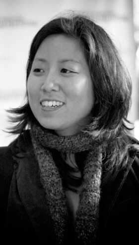 Grace Lee looks away from the camera. She wears a coat and a scarf, and she has medium-length dark hair. Portrait in black and white.