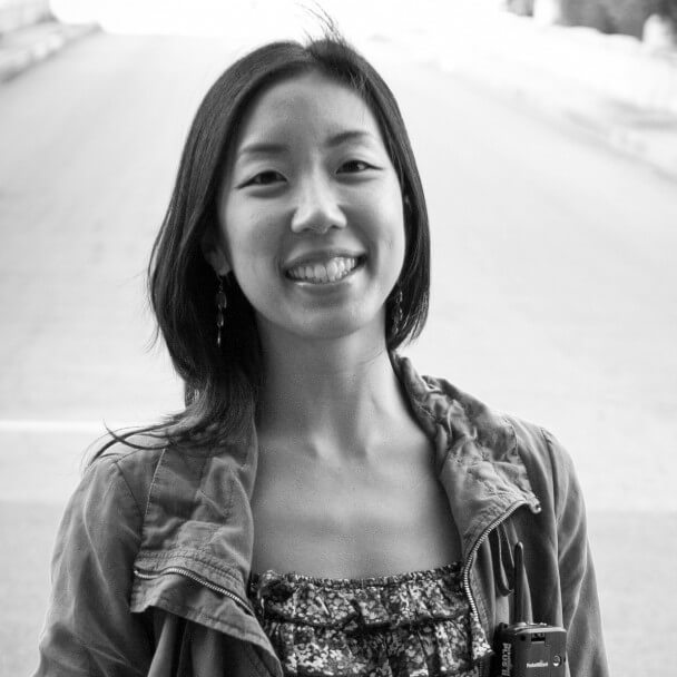 Kathy Huang looking straight ahead and smiling. She has dark, shoulder-length hair and is wearing a jacket and patterned shirt. Black and white portrait.