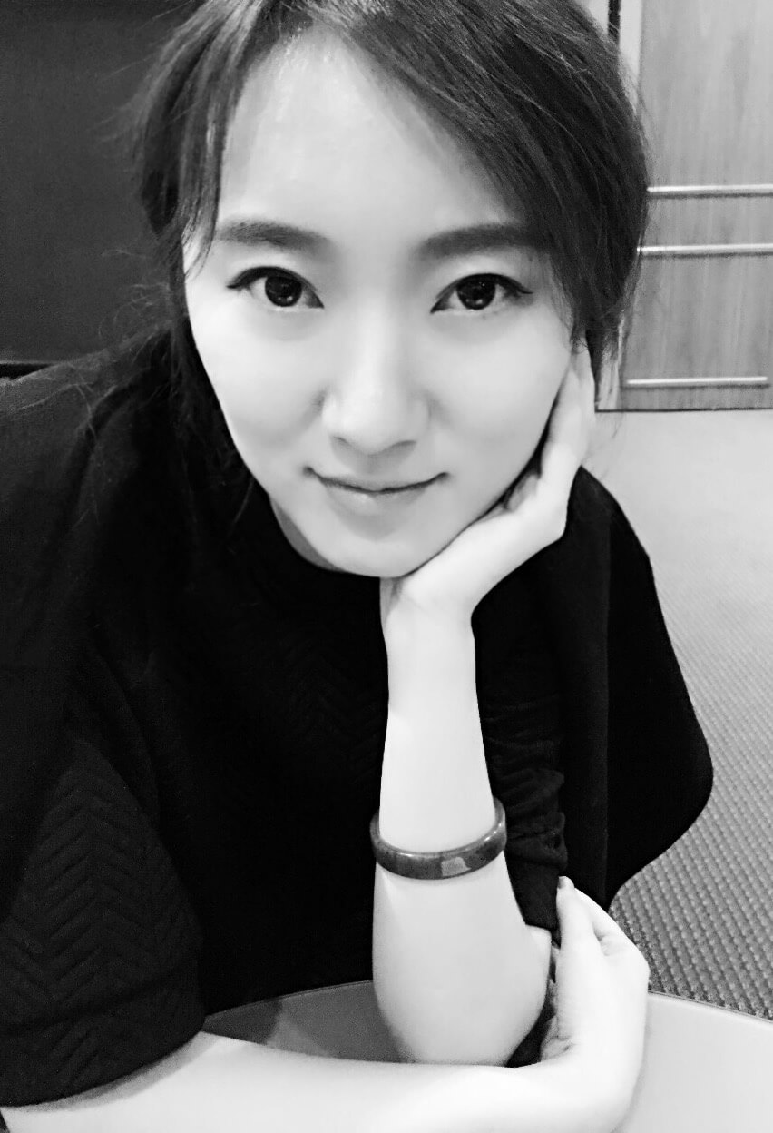 Siyan Liu looking directly ahead. She has dark hair and is wearing a black shirt. She is resting her head on one hand. Black and white portrait.