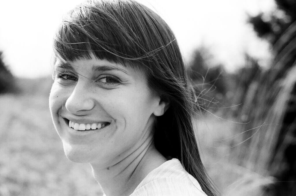 Elaine McMillion looking directly at the camera, smiling, with medium hair and fringe. Black and white portrait, background out of focus.