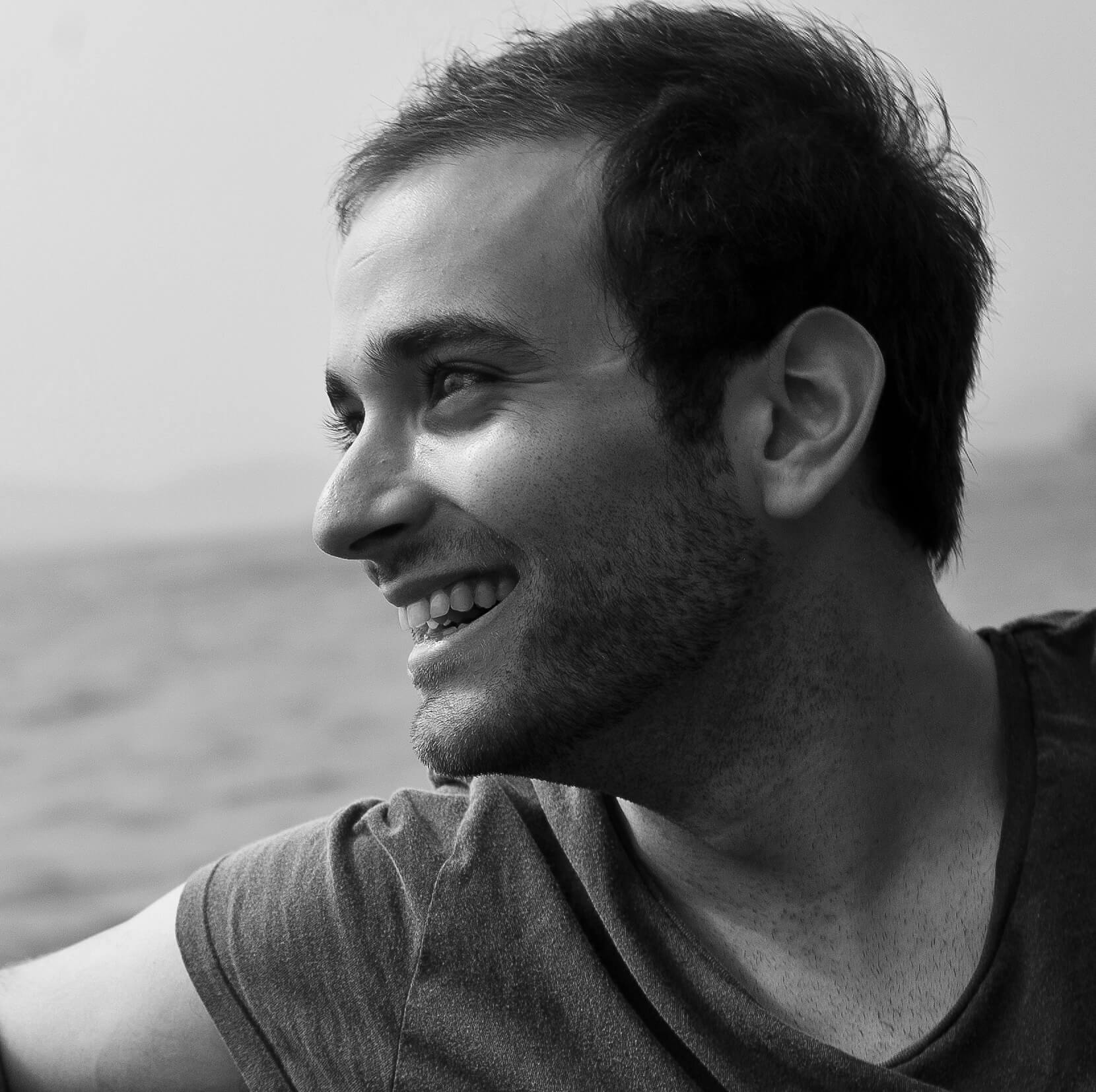 David Osit looking offscreen to his right, smiling. He has short hair and slight stubble. Black and white portrait, with out of focus background.