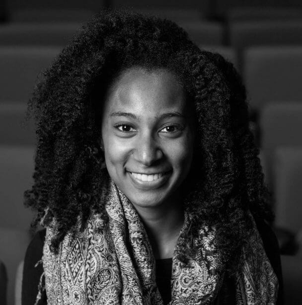 Chelsi Bullard looking directly ahead and smiling. She has very curly, shoulder-length hair and wears a patterned scarf. Black and white portrait.