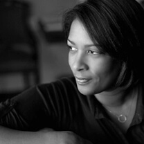 Dawn Porter looking off camera. She is wearing a dark shirt and a circle necklace. Black and white portrait, with out of focus background.