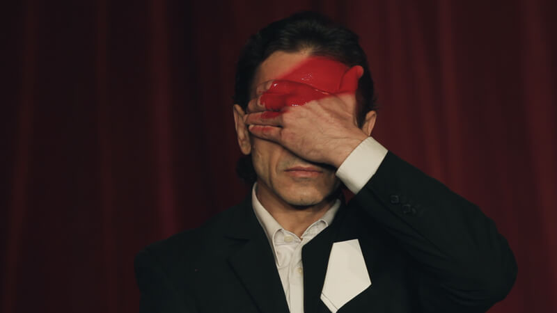 A person with a white shirt and a blazer covers half of their face, their palm, and part of the forehead has a red thick line.