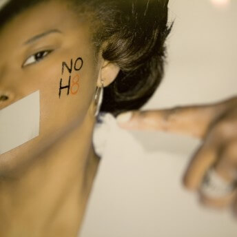 Still from The New Black. A photo of a poster with a picture of a person who has duct tape over their mouth and the words "NO H8" written on their cheek.