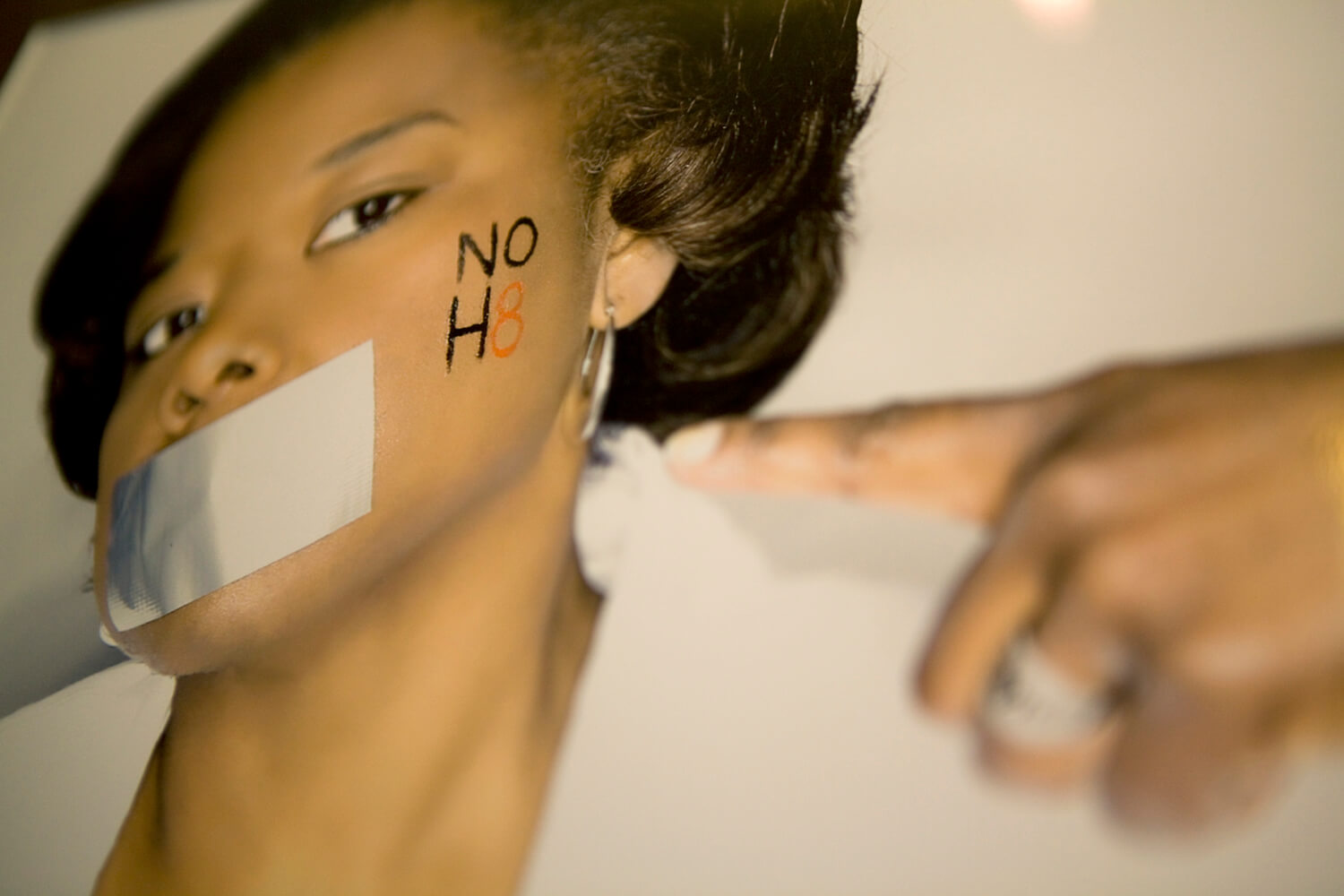 Still from The New Black. A photo of a poster with a picture of a person who has duct tape over their mouth and the words "NO H8" written on their cheek.