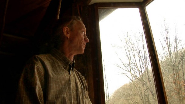 A man with a buttoned shirt looking through a window.