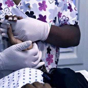 Still from Trapped. Close-up of a nurse wearing gloves and holding a person's hand.