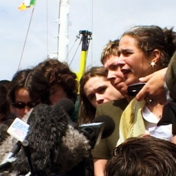 Still form Vessel. A woman is being interviewed, surrounded by microphones and other people.