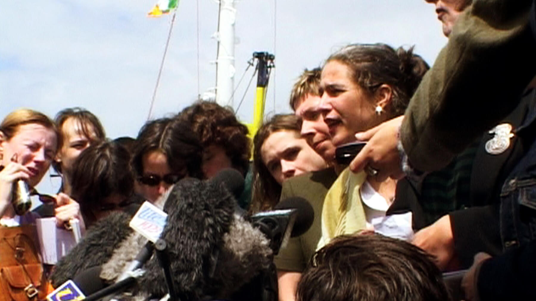 Still form Vessel. A woman is being interviewed, surrounded by microphones and other people.