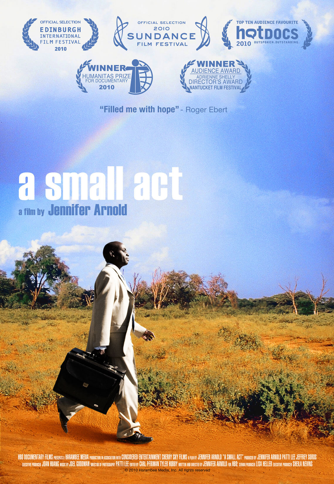 Poster of A Small Act. A man in a white suit is walking with a briefcase in front of an open land with dry grass and a bright blue sky and a rainbow. The graphics on it say the name of the film and the name of the director: Jennifer Arnold.