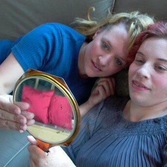 Still from About Face: The Story of Gwendellin Bradshaw. High-angle shot of two women holding a mirror infront of themselves.