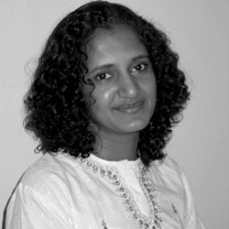 Hemal Trivedi looking at the camera. She has wavy medium-length hair and wears a white embroidered shirt. Portrait in black and white.