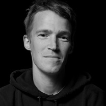 Jason Mann looks directly at the camera. He wears a dark hoodie. Portrait in black and white.