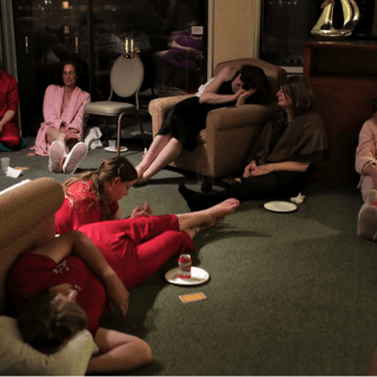 Still from The Pearl. A group of women is sitting on a carpeted floor in a room. Some of them wear robes, and others are not wearing shoes.