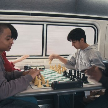 Three teenagers are playing chess on a table.