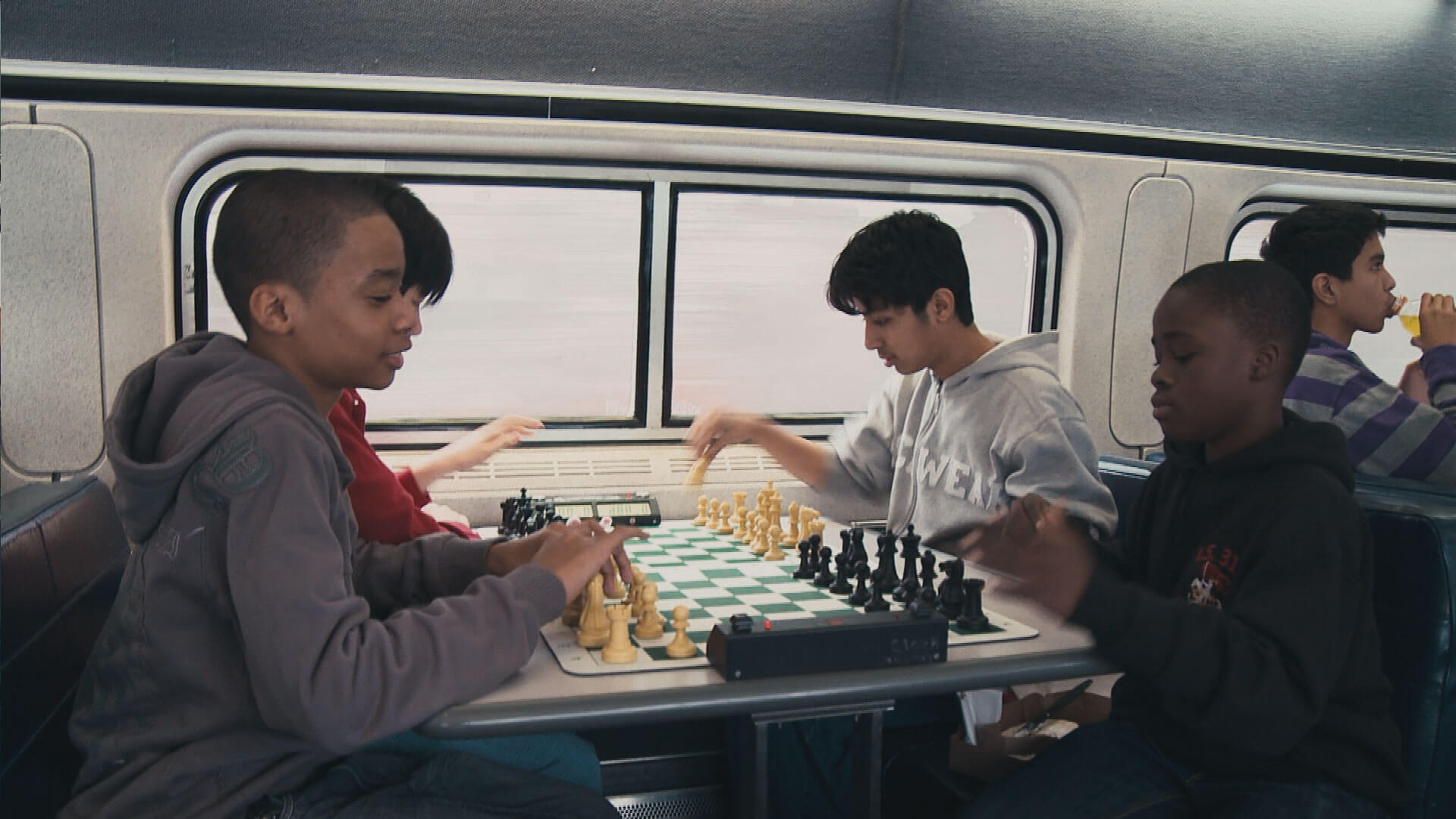 Three teenagers are playing chess on a table.