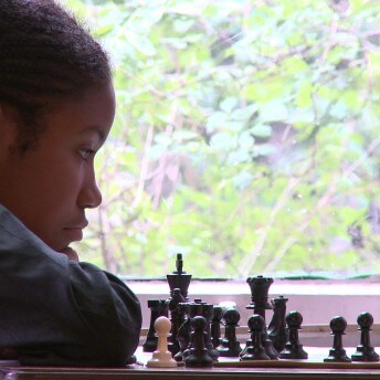 A teenager is reclining her head on her shoulder, while she watches a chess board.