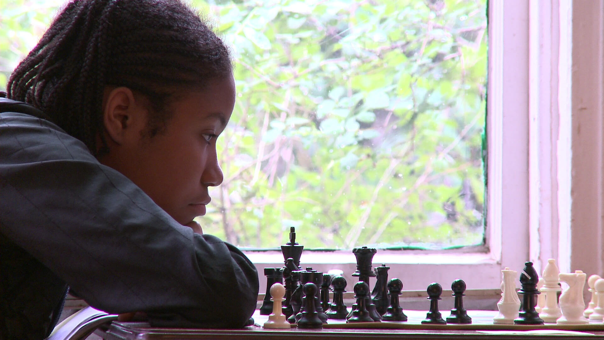 A teenager is reclining her head on her shoulder, while she watches a chess board.