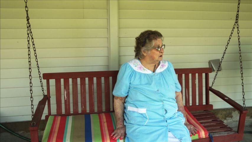 An elderly woman is sitting on a colorful bench.