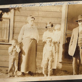 Archive photograph in sepia tone of two adults, with 4 children in front of a house.