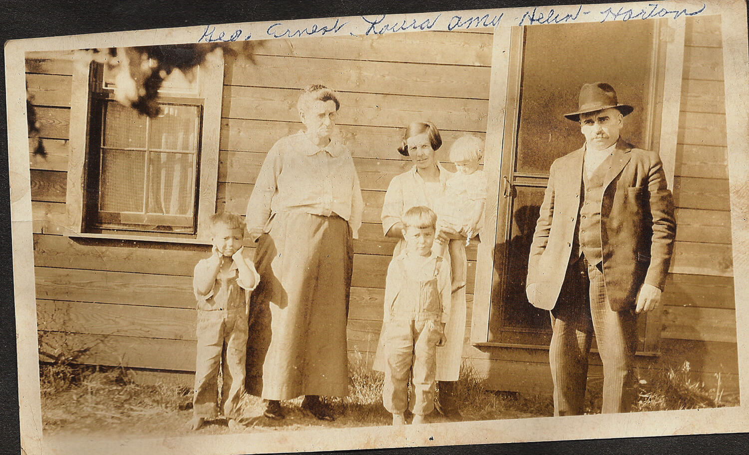 Archive photograph in sepia tone of two adults, with 4 children in front of a house.