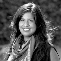 Anayansi Prado looks directly at the camera and smiles. She wears a scarf and has medium-length hair. Portrait in black and white.