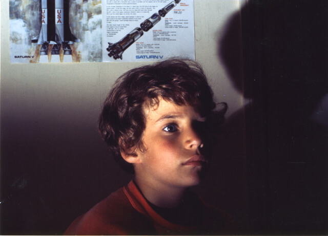 A young boy looks away from the camera. The light illuminates part of his face and leaves the rest in the shadow.