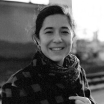 Ashley Sabin looking straight ahead and smiling. She is wearing a patterned shirt and scarf. Black and white portrait, with out of focus background.