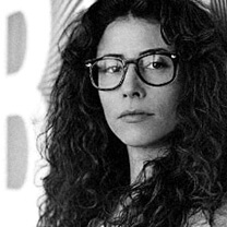 Alma Har’el looks directly at the camera. She wears thick eyeglasses and does not smile. Black and white portrait.