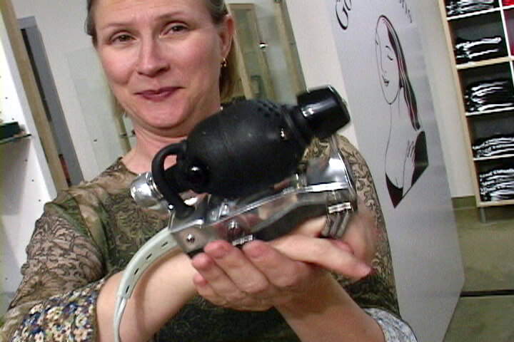 Still from Orgasm Inc. A woman stands in front of the camera presenting a machine that is held in her hands.