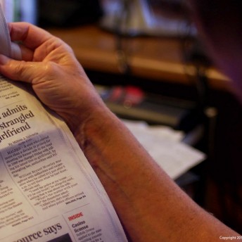 Still from Private Violence. A person's hand is holding the edge of a newspaper, isolating an article titled "Man admits he strangled girlfriend".