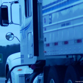 Still from Private Violence. Close-up of the side of a semi-tractor trailer truck. In the blurred background there is a green exit sign for "EXIT 192".