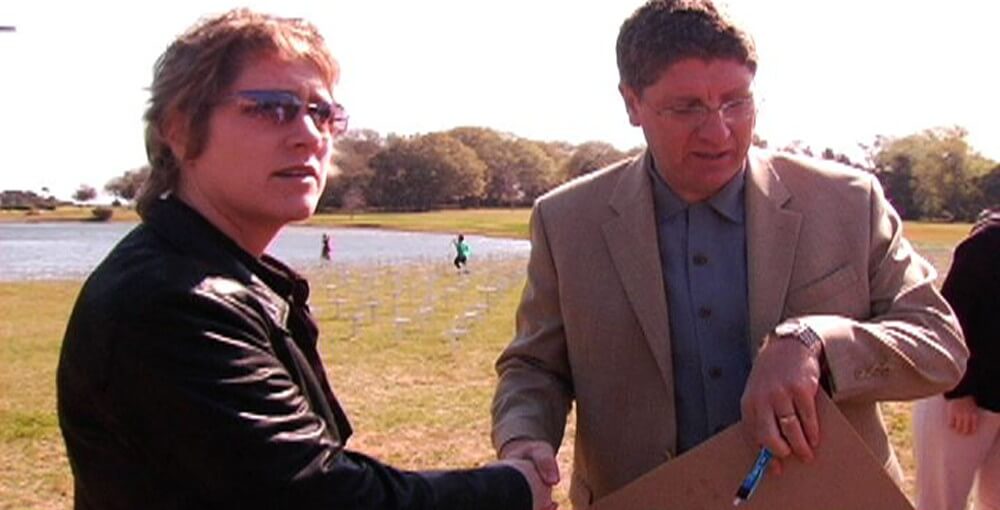 Still from Randall and Me: Together at Last. Two people are standing outside near a lake, shaking hands.