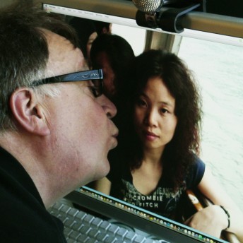 A middle-aged man kisses the screen of a laptop computer. On the screen, there is a photography of a young Chinese woman.