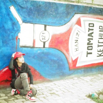Sonita sitting on the ground in front of a wall with a mural of a ketchup bottle.