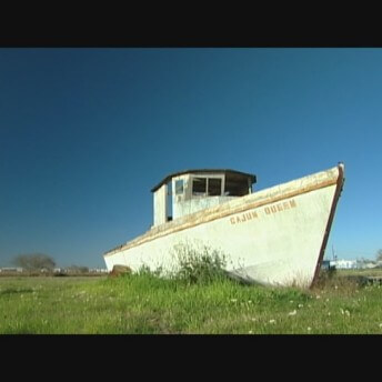 Still of Texas Gold. A white boat set in the middle of a green field.
