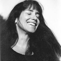 Carolyn Scott tilts her head back and smiles. Her eyes are closed. Portrait in black and white.