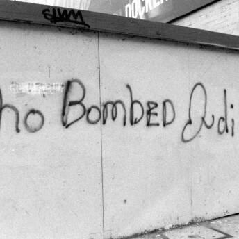 A still from The Forest for the Trees. A black and white photo of graffiti on a concrete wall. The graffiti reads: "Who bombed Judi Bari?"