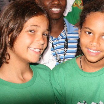 Two kids in green t-shirts smile at the camera. Color photograph.