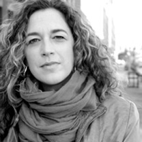 Kristi Jacobson looking at the camera. She wears a scarf around her neck and a jacket. She has curly medium-length hair. Portrait in black and white.
