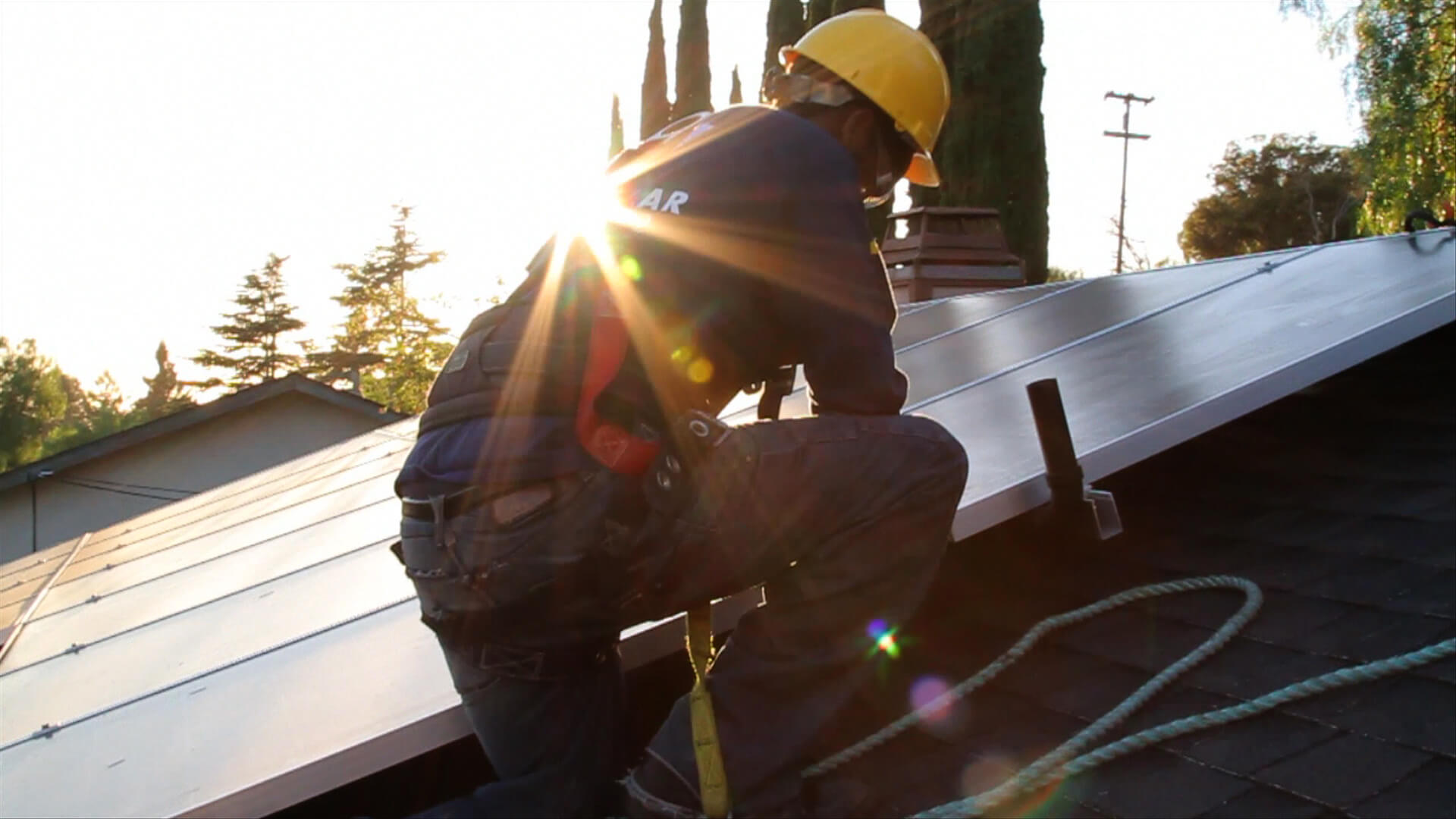 A man is installing solar panels; he wears a helmet, and is stepping down a ladder.