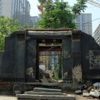 Still from Missing Home: The Last Days of the Beijing Hutongs Weimin Zhang. A damaged building structure and door frame stand among other buildings, trees, and a crane.