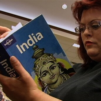 Still from Made in India. A woman with glasses is standing in a bookstore. She is looking at the pages of a book titled, "India".