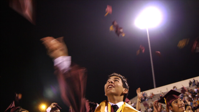 Still from Mariachi High. A young man throws a graduation cap in a crowd of graduates and other people.