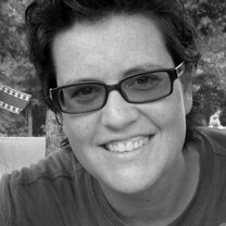 Kim Connell in sun glasses smiles directly at the camera. Black and white portrait.