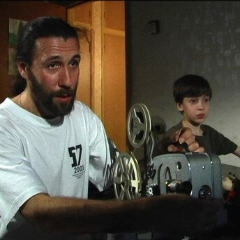 Still from My Perestroika. A man is running an older film projector. A young boy stands beside him.