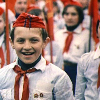 Still from My Perestroika. Rows of children wearing uniforms of white button down shirts, red ties, and red hats.